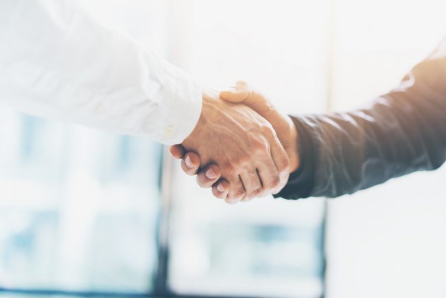 Development partnership Bild mit einem symbolischen Händedruck zwischen zwei Personen, leicht mit einem Lichtreflex in der Mitte