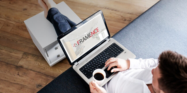 Framence_Digital Twin A man sits relaxed on the sofa with a cup of coffee and works on his laptop. The Framence logo can be seen on the screen, along with a digital environment