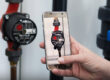 A hand holds a smartphone in front of a water pump; the same pump is shown in focus on the display