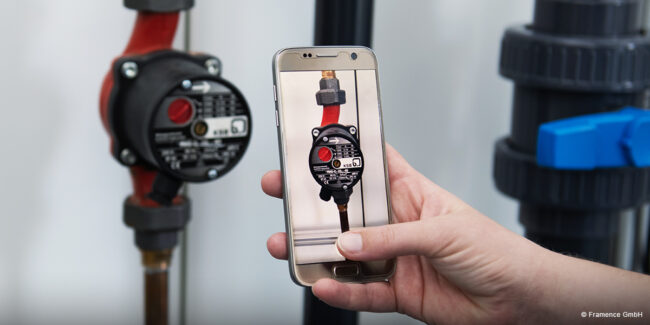 Framence_Blog_Futurelab_Handy A hand holds a smartphone in front of a water pump; the same pump is shown in focus on the display