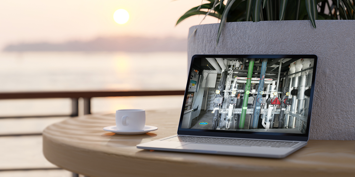 Framence_Blog_Neue_Arbeitswelt Laptop stands on a round wooden table next to a white coffee cup. The screen shows a complex installation of pipes, valves and measuring devices in a technical room. In the background, a blurred landscape with water and sunset, some green plants.