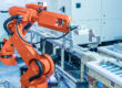 Orange industrial robotic arm operating on an automated conveyor system in a modern manufacturing facility.