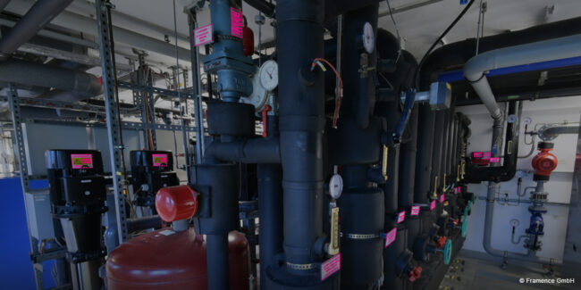Framence_Blog_OCR Interior view of a technical facility with black pipelines, pressure gauges, red safety labels, and various valves in a maintenance room.